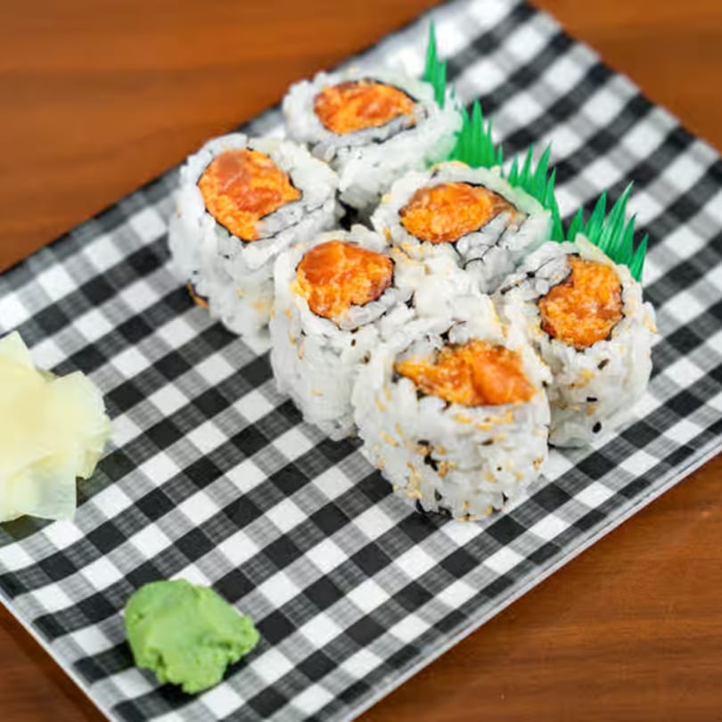 Spicy tuna sushi rolls with wasabi and ginger on a black and white checkered plate.