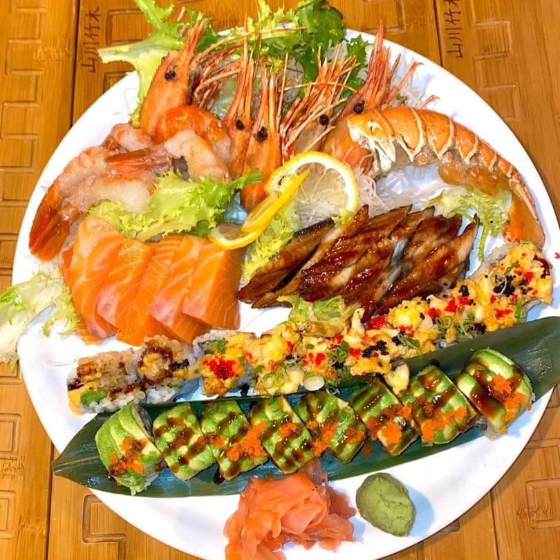 A large white platter of Japanese food including shrimp, salmon sashimi, eel, and various sushi rolls.