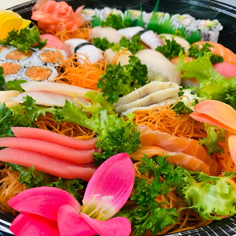 A large platter of assorted sushi, sashimi, and rolls, garnished with lettuce, carrots, and a pink flower.