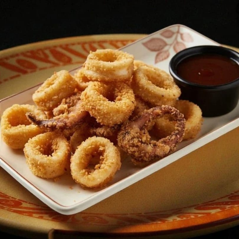 A plate of crispy fried calamari rings and tentacles with a side of dark dipping sauce.