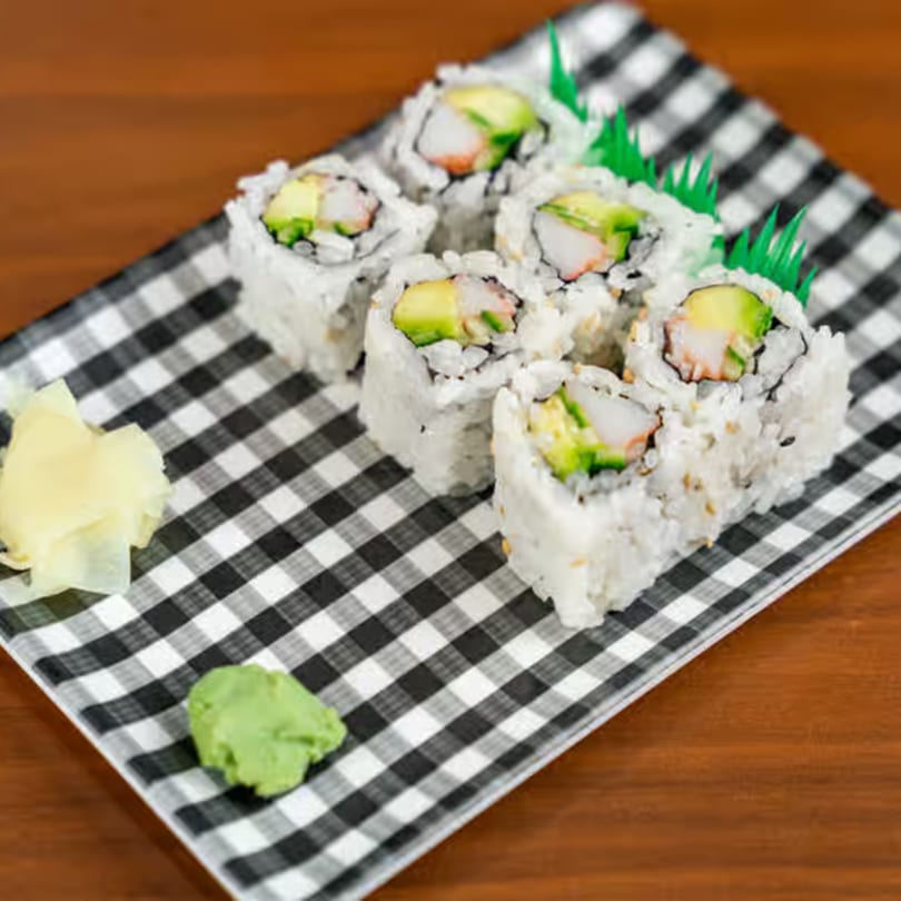 Six California rolls with crab, avocado, and rice, served with ginger and wasabi on a checkered plate.